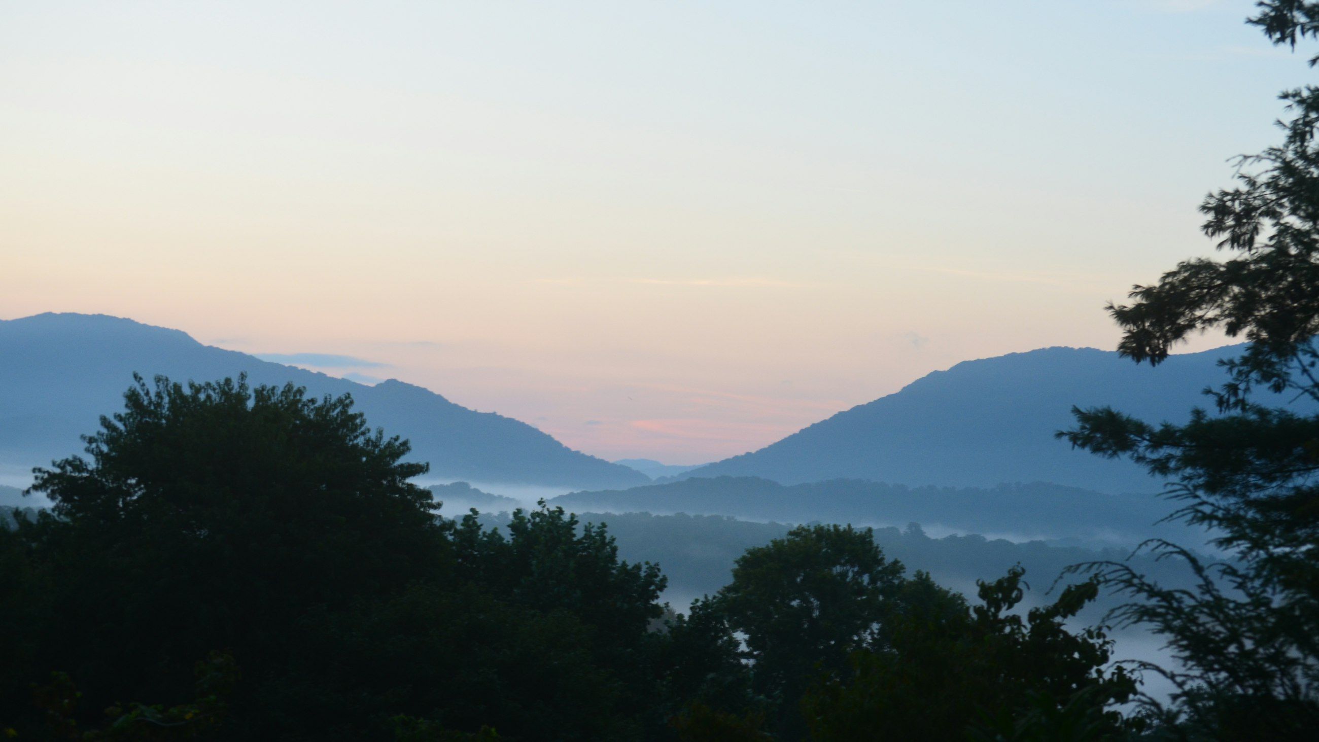 Layered blue mountain ridgelines above a mist-filled valley at dawn, seen from Waynesville